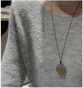 Gros plan du collier pendentif rond en bois minimaliste avec grain naturel sur pull gris