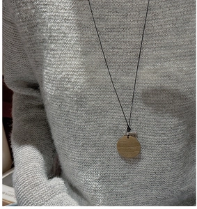 Détail d'un collier pendentif rond en bois sur un pull en maille grise, style épuré