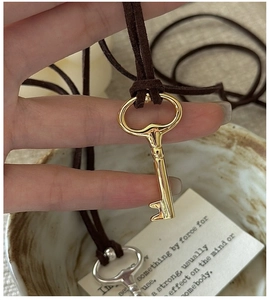 Detail of vintage gold key pendant on brown velvet cord showing smooth metallic texture