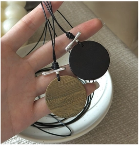 Détail du pendentif rond aspect bois avec cordon noir et fermoir à bascule argenté