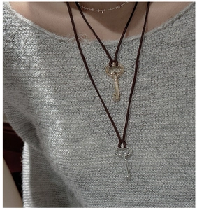 Detail of silver and gold key necklaces worn over a grey knit sweater background