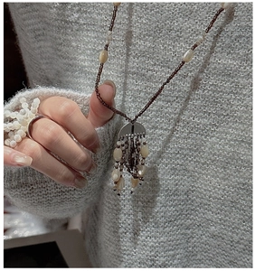 Close-up of beaded brown tassel necklace and pearl ring on a grey knit sweater