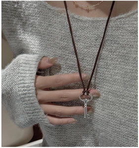 Detailed view of an S925 silver key pendant on a long dark brown cord sweater necklace