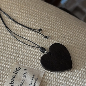 Minimalist S925 silver necklace with black heart wood pendant on a textured fabric base