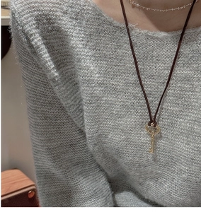 Macro detail of a vintage gold key pendant on a dark brown cord over a grey sweater