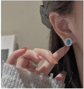 Close-up of S925 sterling silver turquoise stud earrings and textured ring on a model