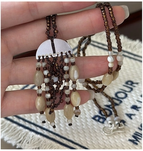 Detail of bohemian woven beaded necklace with brown tassels and matte silver metal piece