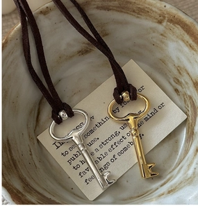 Detailed close-up of retro key pendant necklace with brown suede cord on ceramic plate
