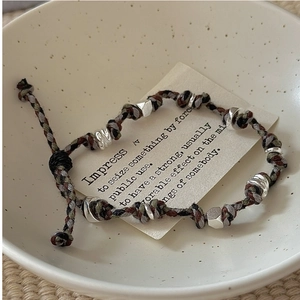 Dettaglio del bracciale in corda intrecciata con perle argentate su un biglietto decorativo