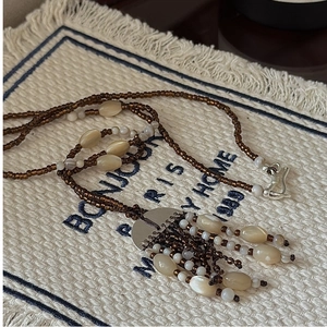 Detail of 925 silver beaded tassel necklace with brown and cream beads on linen