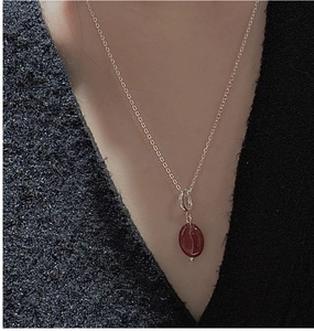 Close-up of a silver necklace featuring a unique red coffee bean resin pendant on a grey sweater