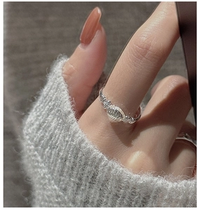 Detailed close-up of a silver shell ring with fine radial stripes on a grey knit background
