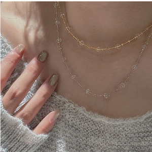 Gros plan de colliers de perles dorées et argentées superposés sur un pull gris