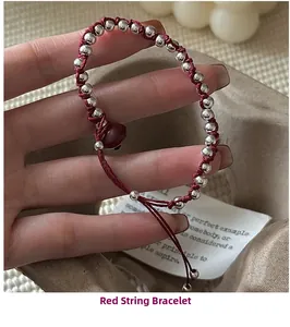 Macro detail of hand-woven red string bracelet with silver beads and heart charm