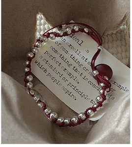Macro detail of hand-woven red cord bracelet with S925 sterling silver beads decoration