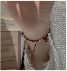 Detailed view of handmade red braided silver bead bracelet on a wrist against knitwear