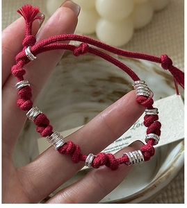 Macro shot of handmade red braided cord bracelet with silver rings and tassel detail