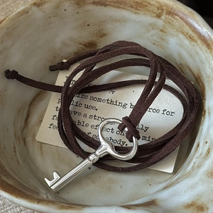 Vintage S925 silver key pendant necklace with dark brown suede cord on a ceramic dish