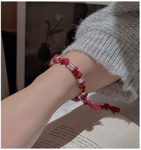 Detail of red braided cord bracelet with silver threaded rings on a model wrist