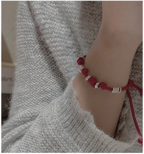 Close-up of red braided rope bracelet with silver layered rings on a woman's wrist