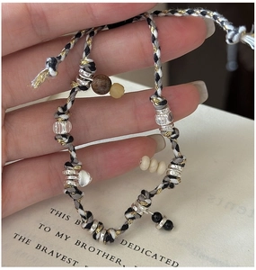 Macro detail of hand-woven bracelet with silver heart charm and assorted beads over a book