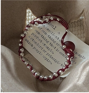 Detail of hand-woven deep red rope bracelet with silver beads in a star gift box
