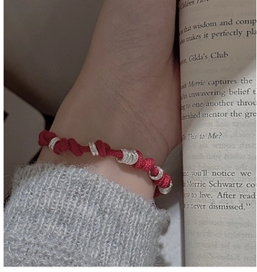 Detailed view of red woven rope bracelet with tiered silver rings on a model's wrist