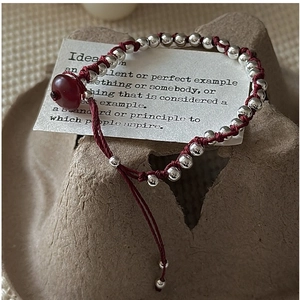 Macro detail of red woven rope bracelet with polished silver beads and agate charm