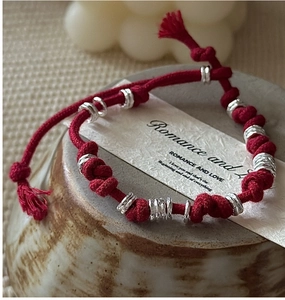 Close-up of handmade red string bracelet with silver beads on ceramic dish decoration