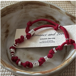 Detail of red braided cord bracelet with textured silver rings in a ceramic bowl