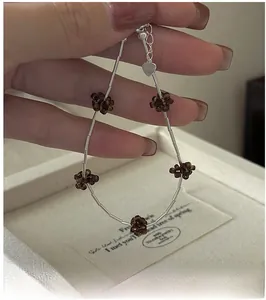 Detail of S925 silver beaded bracelet with brown floral charms and a heart pendant