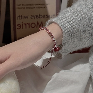 Minimalist red woven bracelet with silver beads and a red heart charm on wrist
