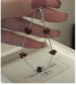 Detail of silver beaded bracelet with brown floral charms and heart-shaped pendant