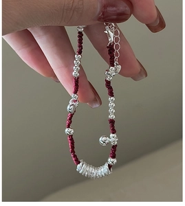 Dettaglio di bracciale in corda rossa con perle d'argento, campanellino e chiusura a moschettone
