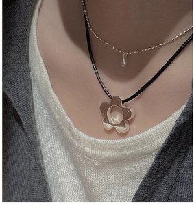 Close-up of S925 silver flower pendant necklace layered with a black cord on a white shirt