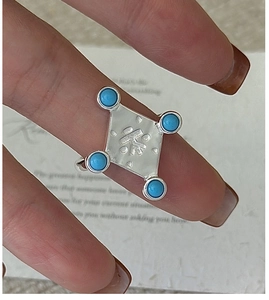 Macro shot of silver ring featuring a square face with four turquoise stones and engraving