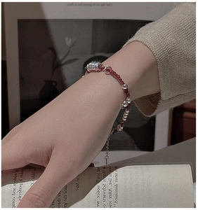 Dettaglio di un bracciale in corda rossa con perle d'argento su sfondo vintage e libro