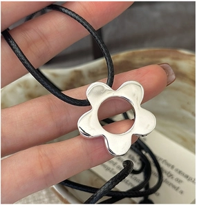 Close-up of minimalist S925 silver flower pendant with black cord necklace held by hand
