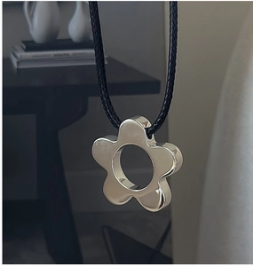 Macro shot of silver flower pendant with polished finish on a black braided rope necklace
