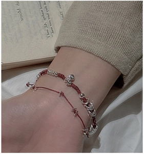 Dettaglio di bracciali in argento S925 con cordoncino rosso indossati su un maglione