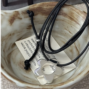 Close-up of minimalist silver flower pendant necklace on a textured ceramic bowl