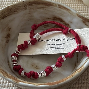 Handmade red string bracelet with silver rings in a vintage ceramic bowl display
