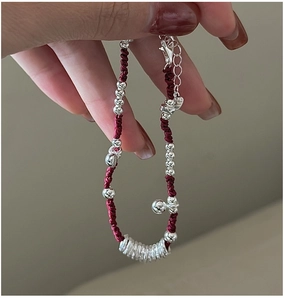 Dettaglio del bracciale a cordino rosso intrecciato con perline d'argento e campanellino