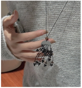 Détail du collier ethnique avec cordons tressés noirs et perles sur pull gris