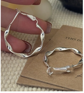 Macro detail of S925 sterling silver hoop earrings with a twisted wave texture design
