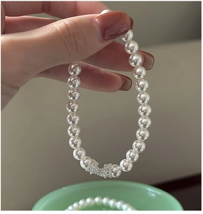 Gros plan d'un bracelet de perles blanches avec fermoir en argent texturé sur une main