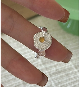 Macro detail of a silver daisy ring featuring a yellow center and hammered texture band