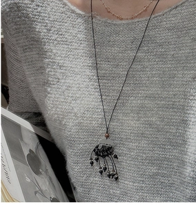 Détail d'un collier long ethnique vintage avec pampilles de perles noires sur pull gris