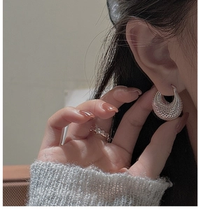 Détail de boucles d'oreilles créoles argentées avec texture en maille creuse sur modèle