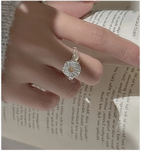 Detail of S925 silver daisy flower ring with yellow gemstone on a hand over a book